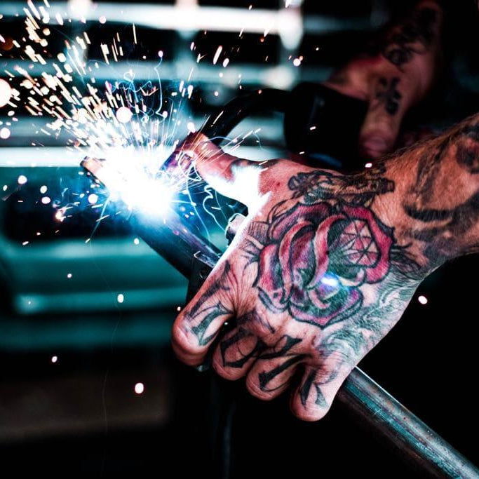 Tätowierte Hand beim Schweißen von Metall mit Funkenflug in Werkstattumgebung