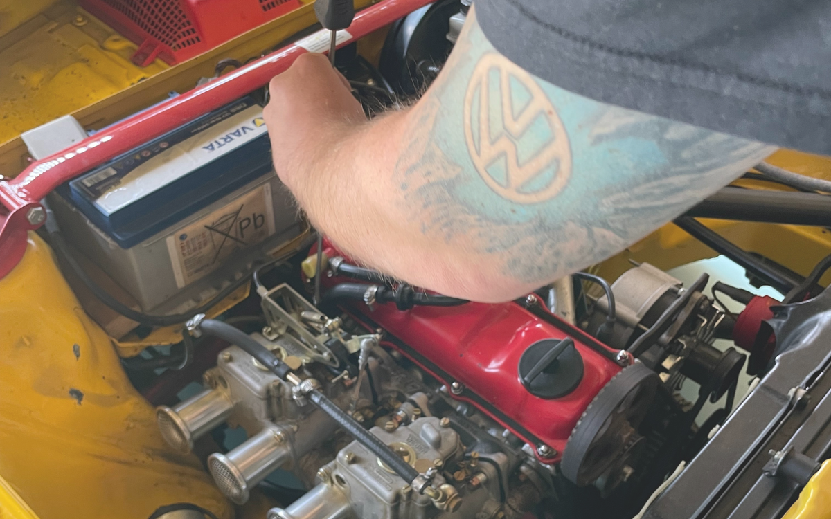 Mechaniker mit VW-Tattoo arbeitet am luftgekühlten VW-Motor im gelben Oldtimer