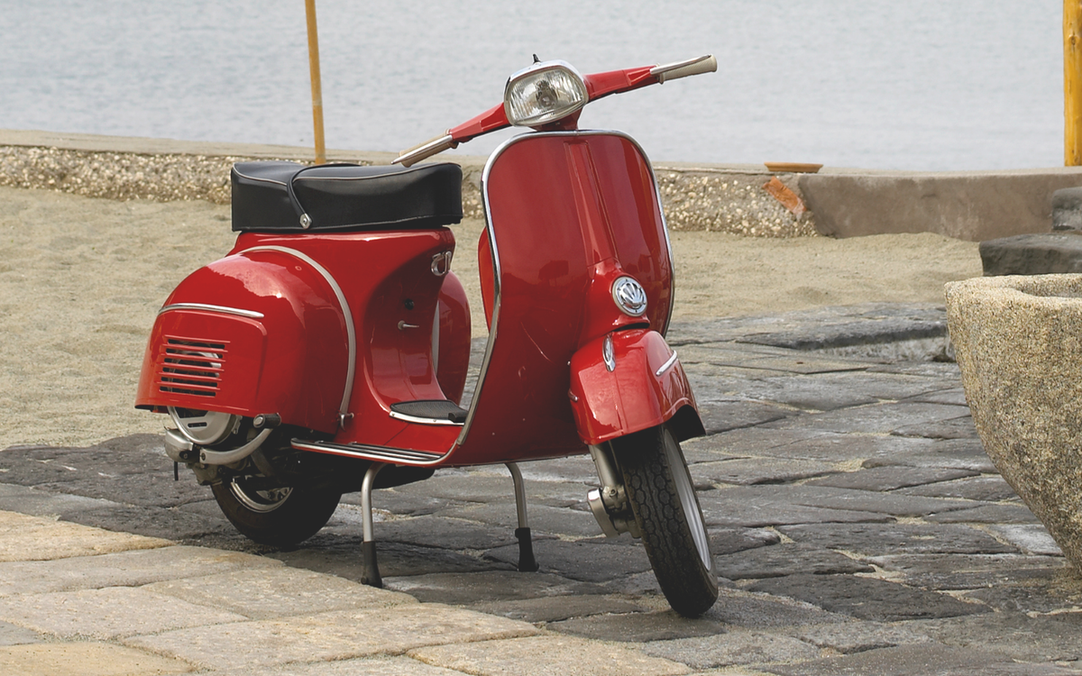 Roter klassischer Motorroller mit VW-Logo am Seeufer auf Kopfsteinpflaster